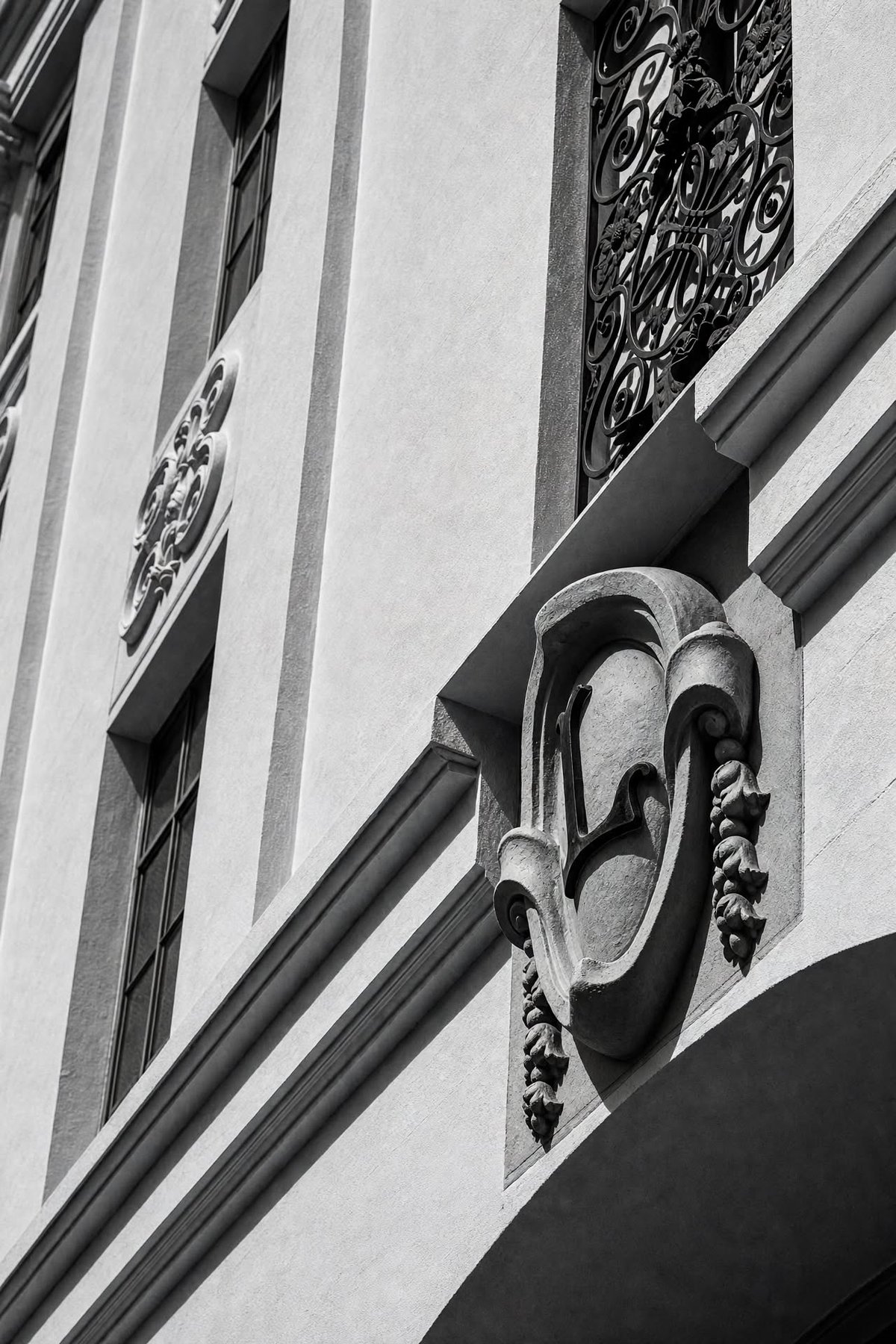 Cast ornament on the Cota Street facade: a scrolled cartouche carrying the letter L, framed by fruit swags, beneath a wrought-iron grille.